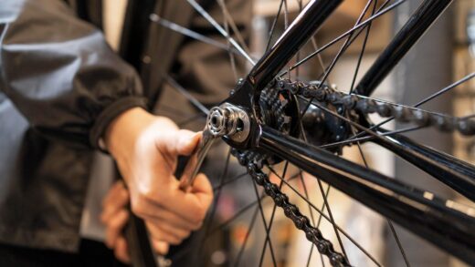 a rear wheel and chain of a bike, and a hand using a wrench to tighten the nut